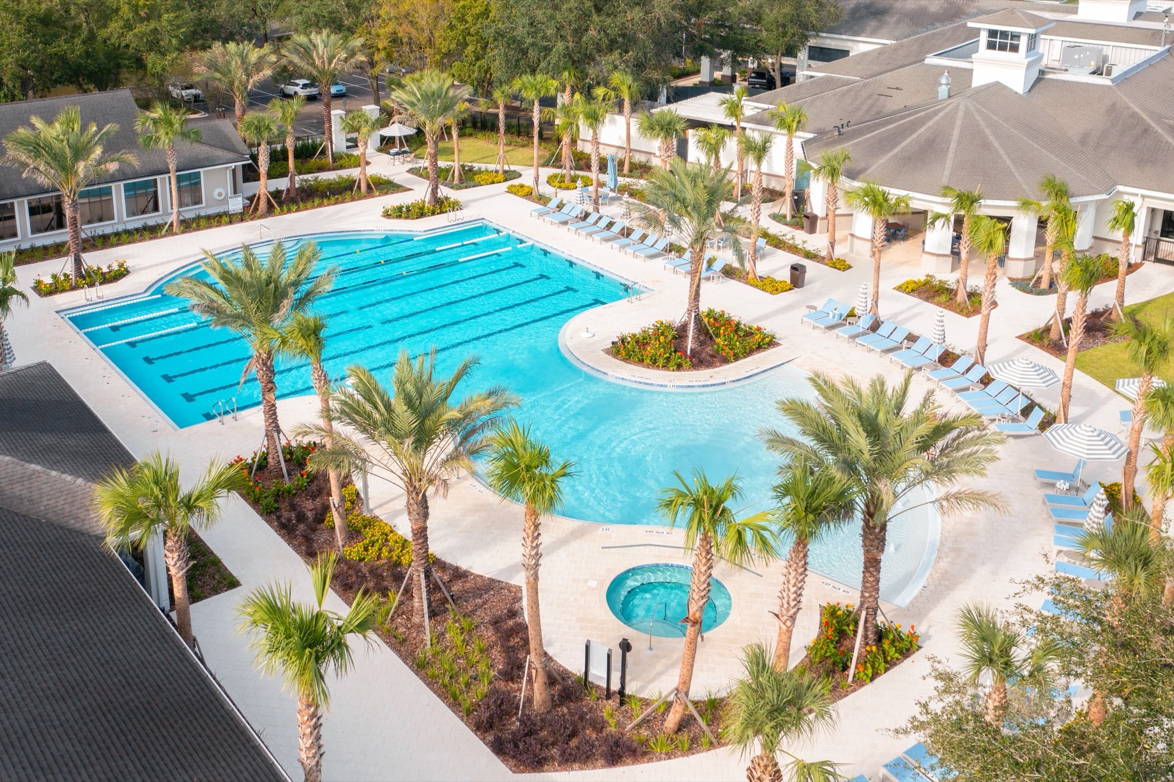 An aerial view of a palm-lined HOA pool with lap lanes, a spa and the clubhouse beside it.