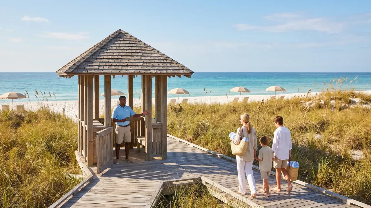 A beach attendant in a wooden gazebo on a boardwalk, with a family walking toward the sand.